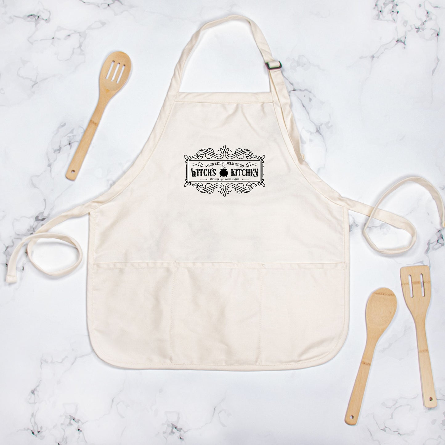 Beige apron with 'Baker's Kitchen' text on a marble surface with wooden utensils.